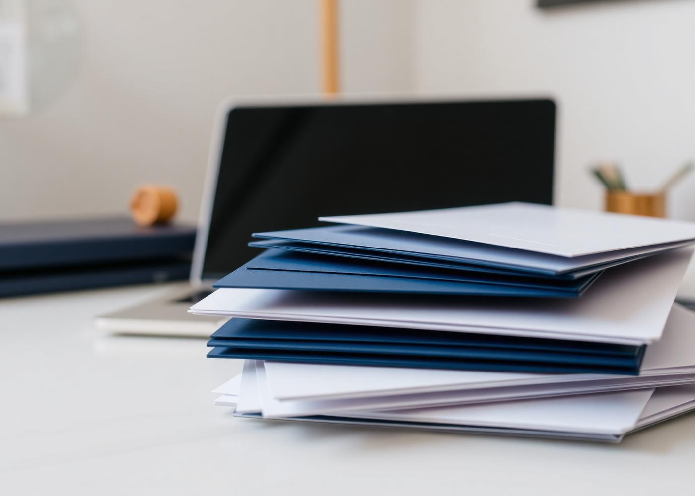 Stack of business letters and documents beside a laptop on a clean desk